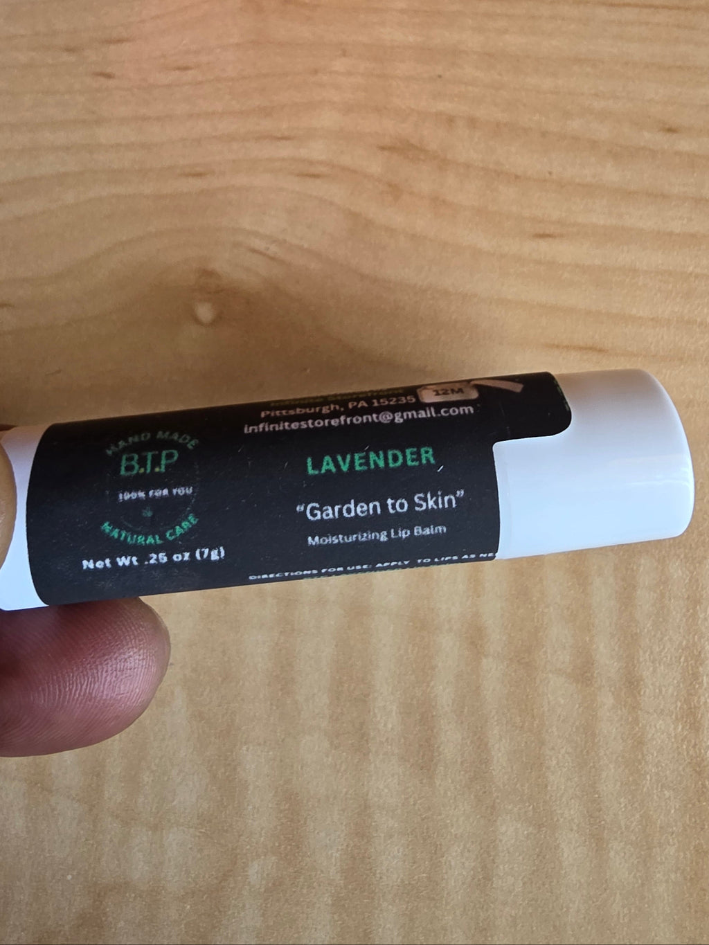 Lip balm tube held by a hand on a wooden surface