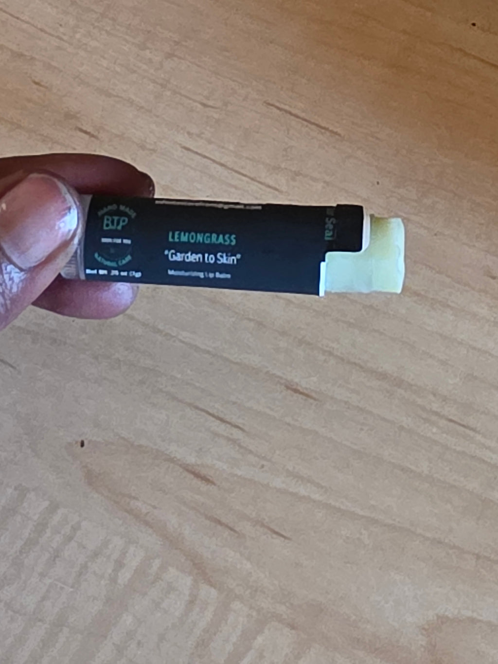 Hand holding a black and white product tube on a wooden surface