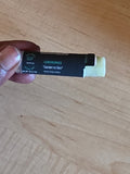 Hand holding a black and white product tube on a wooden surface