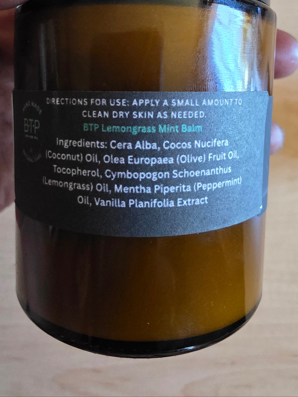 Hand holding a brown jar with a label on a wooden surface