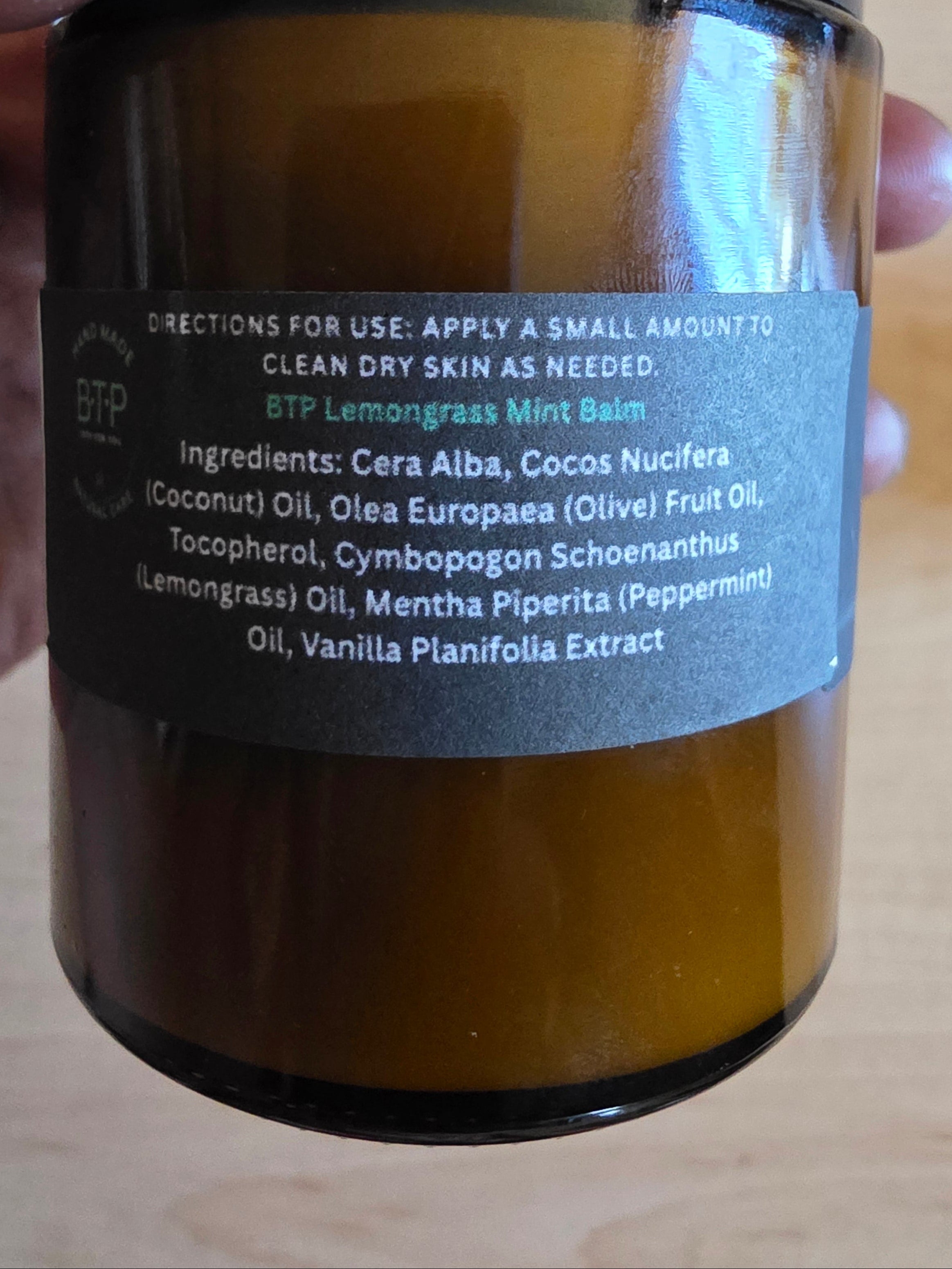 Hand holding a brown jar with a label on a wooden surface