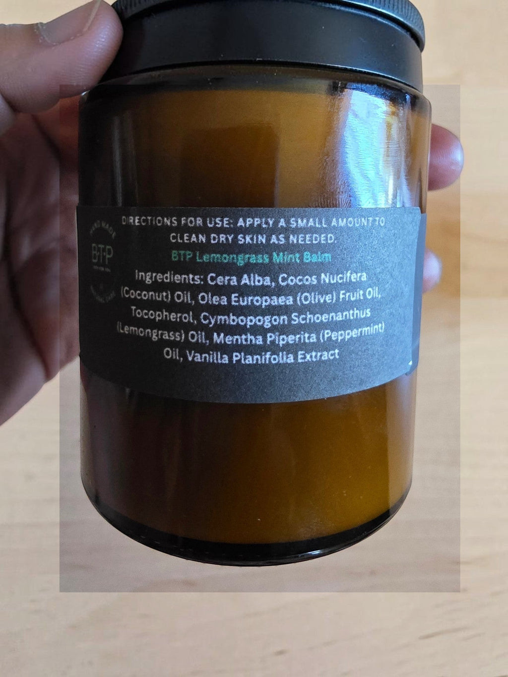 Infinite Storefront B.T.P handmade lemongrass and mint moisturizing body balm in an amber glass jar held in hand.