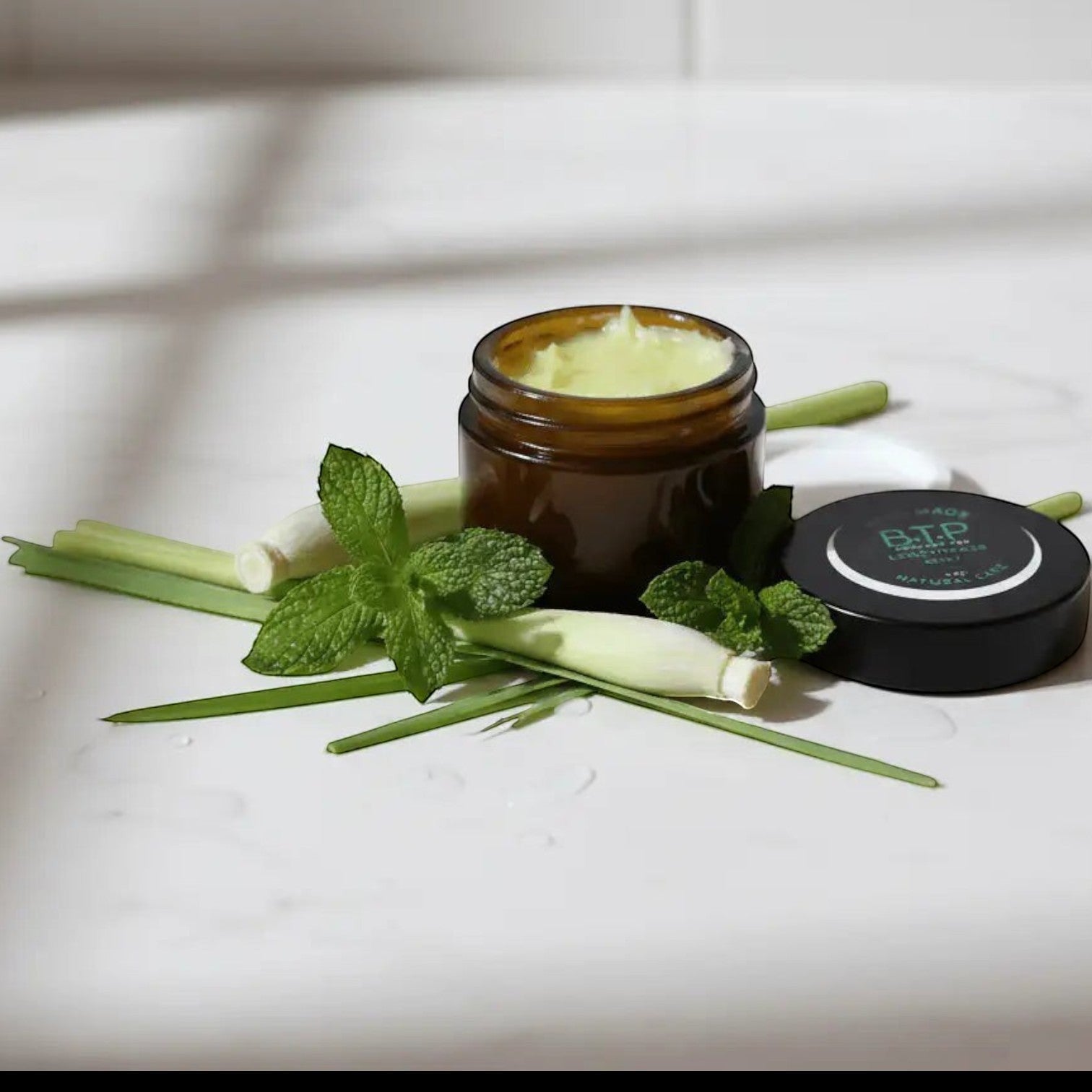 Infinite Storefront B.T.P handmade moisturizing body balm in an amber jar with fresh lemongrass and mint leaves.