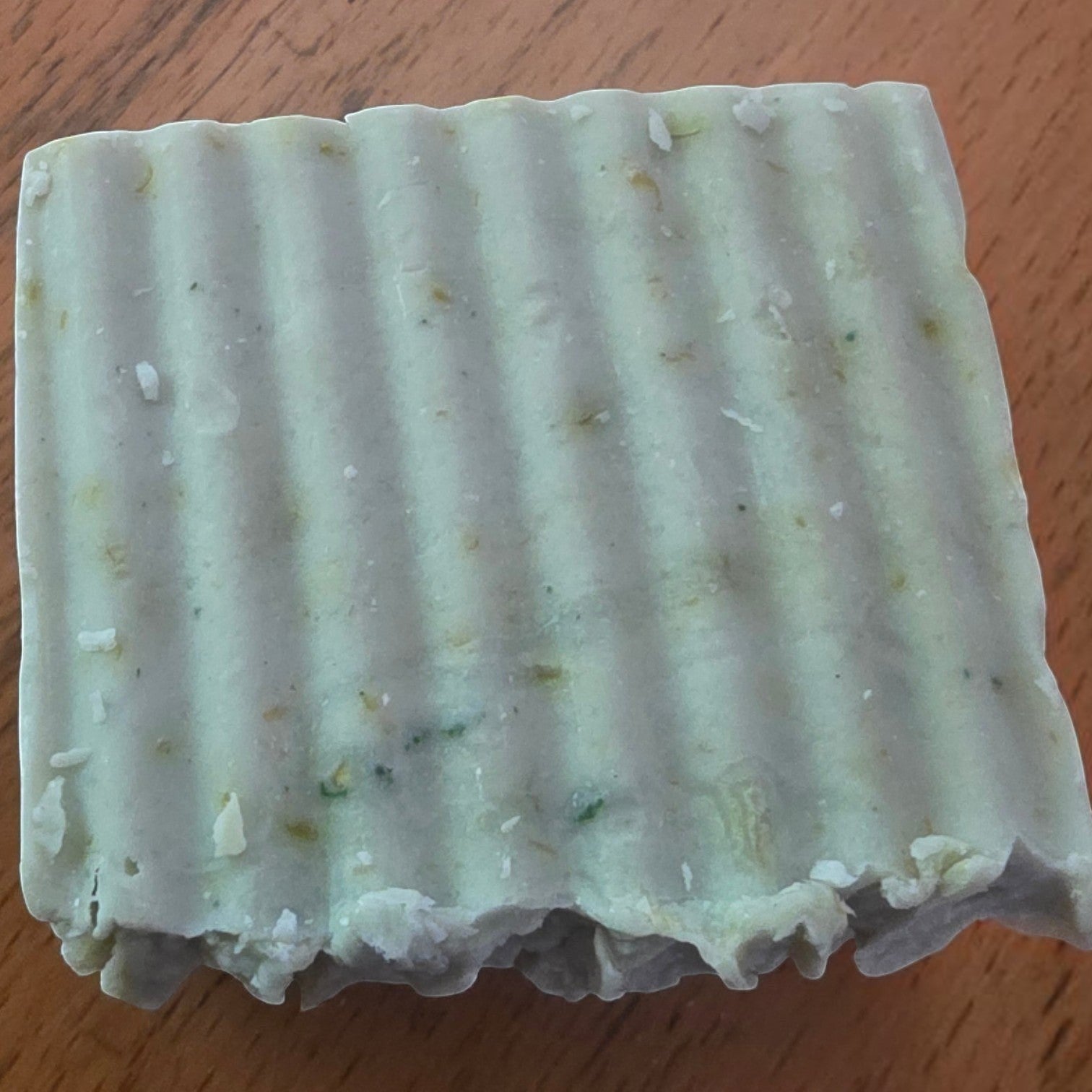 Close up of Cucumber Bliss handmade soap with a pale green textured surface and botanical flecks.