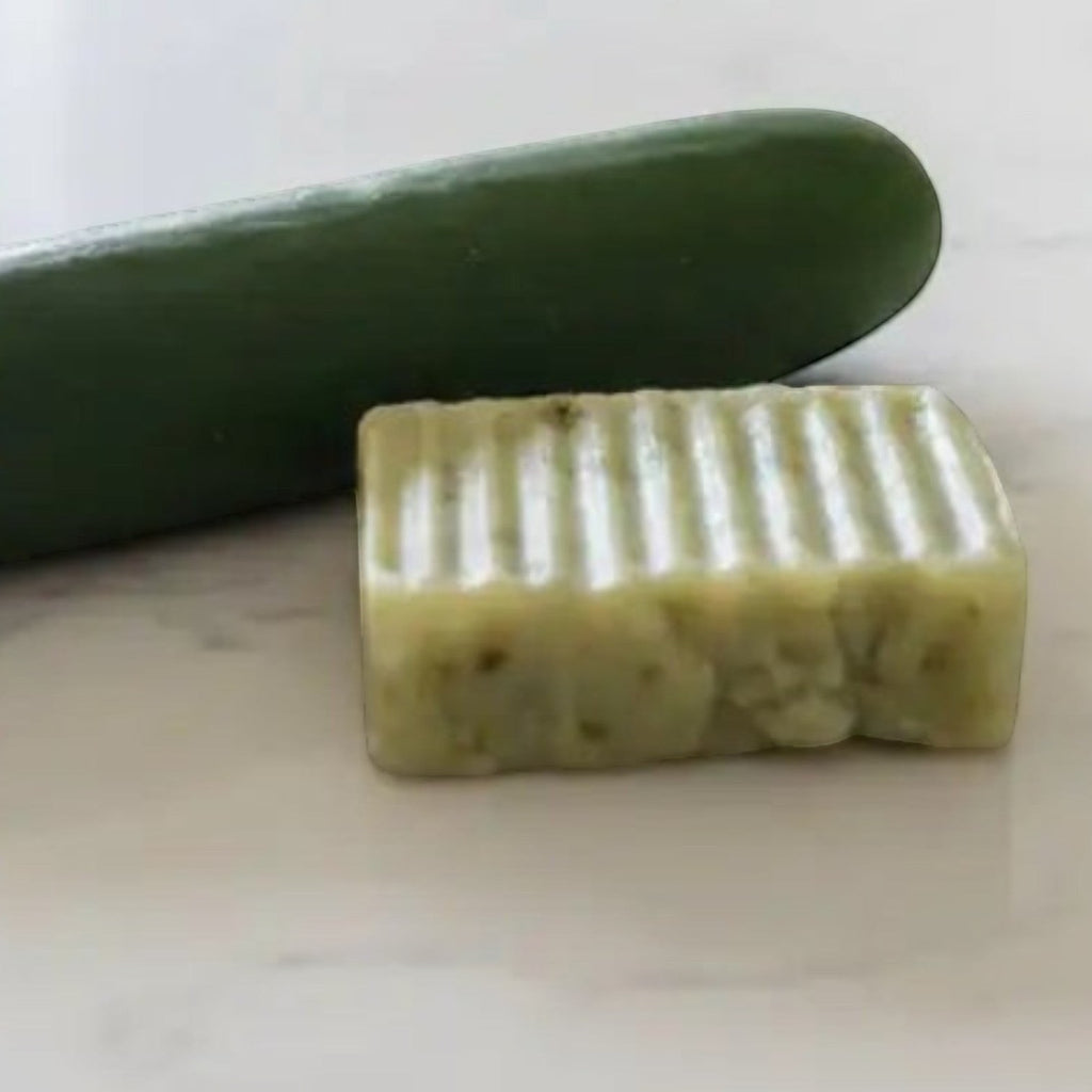 Cucumber Bliss handmade soap bar beside fresh cucumber on a white marble countertop for a refreshing spa inspired experience.