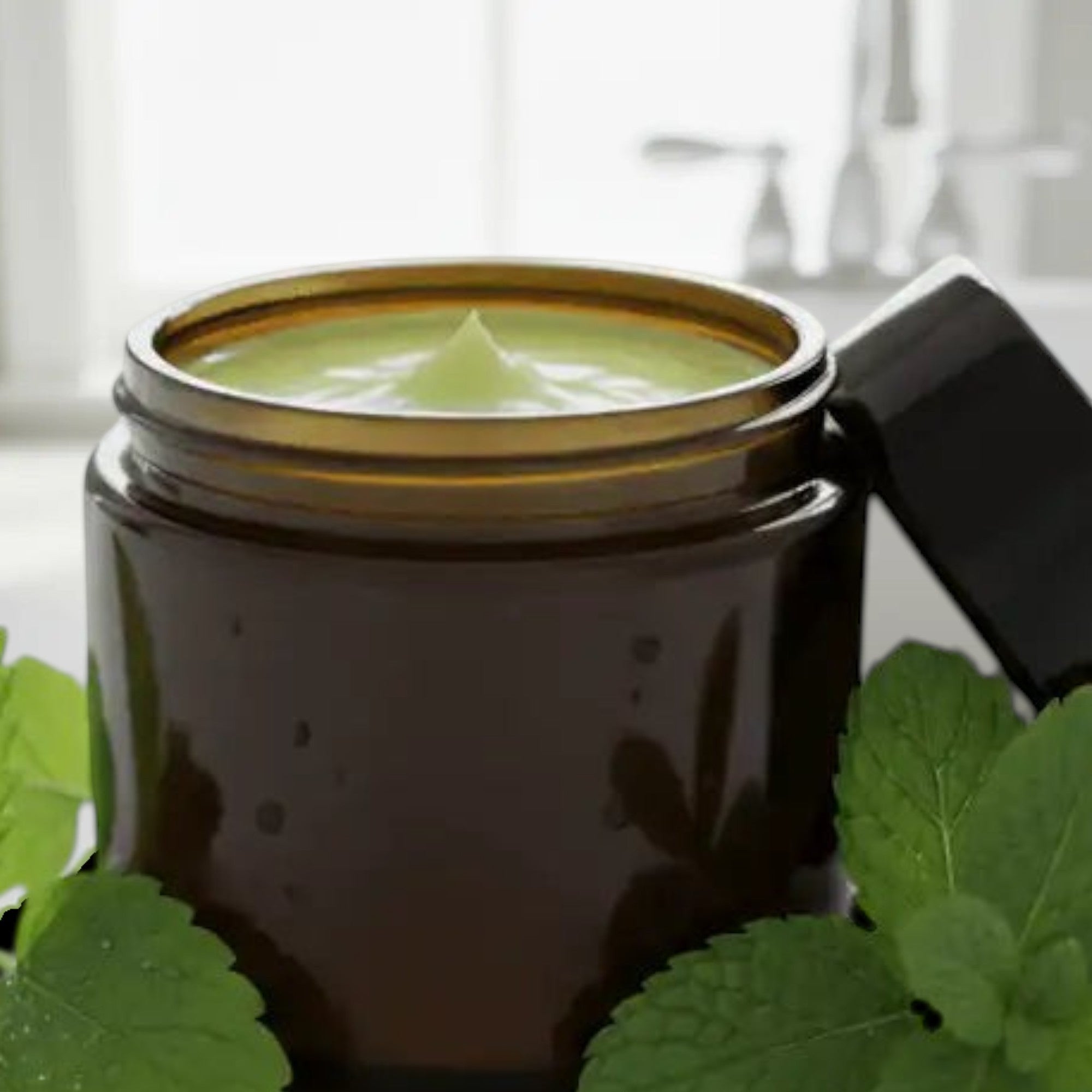 Infinite Storefront lemon balm and peppermint body balm in an amber glass jar with fresh mint leaves on a white counter.